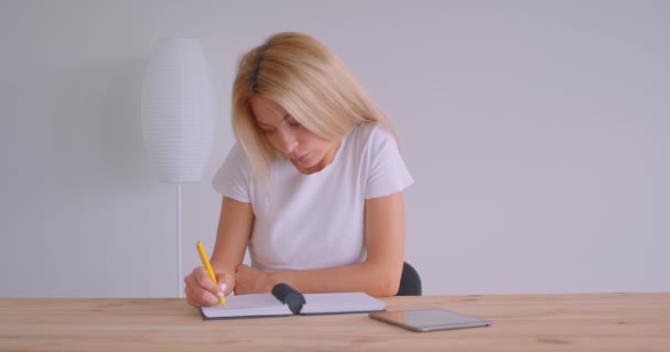 Retrato de close-up de mulher de negócios loira caucasiana adulta usando o tablet e tomando notas dentro de casa no escritório na mesa — Vídeo de Stock