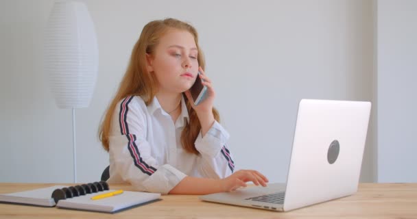 Gros plan portrait de jeune jolie fille caucasienne ayant un appel téléphonique au téléphone en utilisant l'ordinateur portable à l'intérieur dans l'appartement — Video