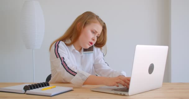 Κοντινό πλάνο του νεαρού όμορφο καυκάσιο κορίτσι που έχει ένα τηλεφώνημα στο τηλέφωνο πληκτρολογώντας στο φορητό υπολογιστή σε εσωτερικούς χώρους στο διαμέρισμα — Αρχείο Βίντεο