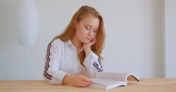 Closeup portrét mladé bělošské dívky studující a čteš knihu uvnitř bytu — Stock video