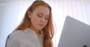 Genç güzel beyaz kız dizüstü bilgisayar kullanarak fotoğraf makinesi sevimli daire içinde kanepede kapalı oturan neşeli gülümseyen görünümlü