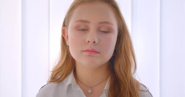 Närbild porträtt av unga ganska kaukasiska flicka tittar på kameran inomhus i vita rummet — Stockvideo
