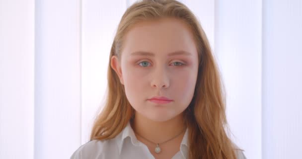 Портрет крупным планом молодой довольно длинношерстной белой девушки, смотрящей на камеру в белой комнате — стоковое видео