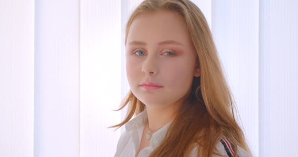 Closeup side view portrait of young pretty caucasian girl turning and looking at camera indoors in the white room — Stock Video