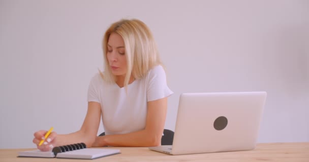 Retrato de cerca de una mujer de negocios rubia caucásica adulta usando el portátil y tomando notas en el interior de la oficina — Vídeo de stock