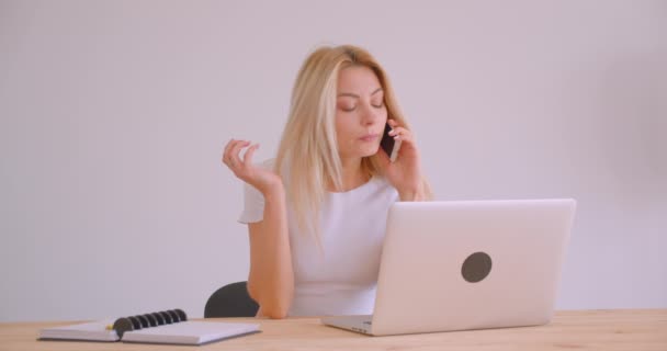 Portrait rapproché d'une femme d'affaires blonde caucasienne adulte utilisant l'ordinateur portable ayant un appel téléphonique à l'intérieur du bureau au bureau — Video