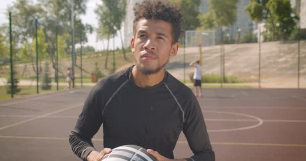 Closeup retrato de jovem afro-americano bonito jogador de basquete masculino jogando uma bola em um aro ao ar livre — Vídeo de Stock