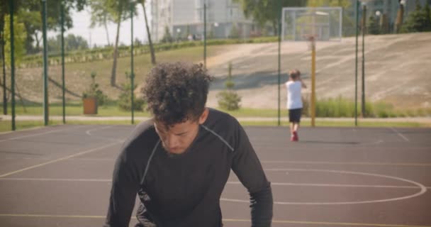 Retrato de primer plano del joven jugador de baloncesto afroamericano deportivo lanzando una pelota en un aro al aire libre — Vídeo de stock