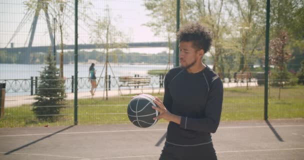 Primer plano vista lateral retrato de joven guapo afroamericano jugador de baloncesto masculino lanzando una pelota en un aro al aire libre — Vídeo de stock