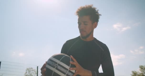 Крупный план портрета молодого опытного африканского баскетболиста, бросающего мяч в кольцо на открытом воздухе — стоковое видео