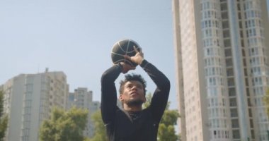 Genç sportif African American erkek basketbol oyuncusu arka planda binalar ile mahkeme açık havada bir çember içine bir top atma portre