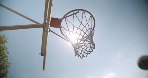 Retrato de primer plano de la pelota de baloncesto lanzada en un aro al aire libre en la cancha con luz solar brillante — Vídeos de Stock