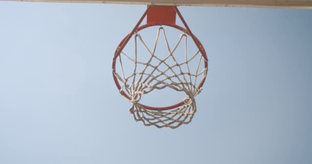 Primer plano de abajo hacia arriba ver el retrato de pelota de baloncesto que se lanza en un aro al aire libre en la cancha con el cielo en el fondo — Vídeos de Stock