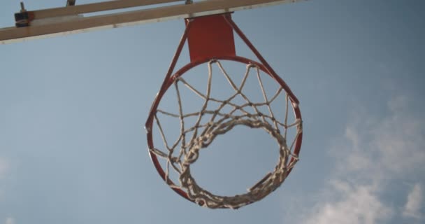 Primer plano de abajo hacia arriba ver retrato de pelota de baloncesto que se lanza en un aro al aire libre en la cancha con cielo nublado — Vídeo de stock