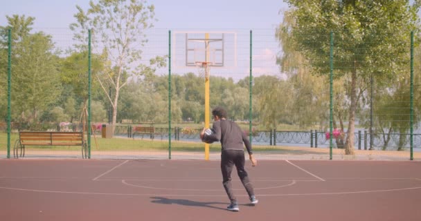 Retrato del jugador de baloncesto afroamericano deportivo lanzando una pelota en un aro al aire libre en la cancha en la ciudad urbana — Vídeo de stock