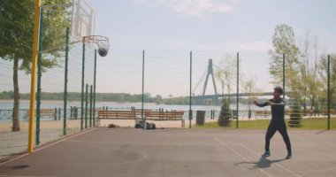 Sportif neşeli Afrikalı Amerikan erkek basketbol oyuncusu bir çember içine bir top atma ve arka planda köprü ile kentsel şehir açık havada mahkemede zaferle kutluyor portresi