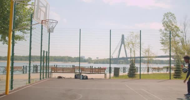 Sportif çekici afro-amerikan erkek basketboloyuncusu bir çember içine bir top atma ve arka planda köprü ile şehir açık havada sahada kutluyor Portresi — Stok video