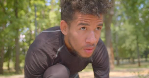 Lähikuva muotokuva nuori urheilullinen afrikkalainen mies lenkkeilijä valmistautuu juosta puistossa määritetään ulkona — kuvapankkivideo