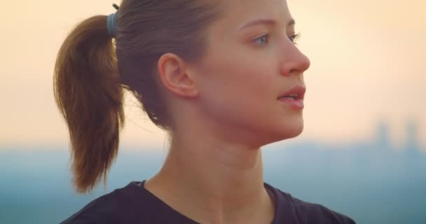 Closeup portré fiatal motivált sportos női kocogó egy fekete póló nézi a gyönyörű naplemente a szabadban — Stock videók
