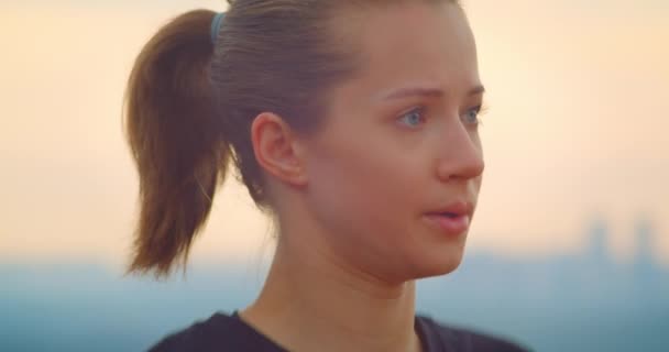 Крупный план портрета молодой мотивированной спортивной бегуньи в черной футболке, разогретой и смотрящей на красивый закат на открытом воздухе — стоковое видео
