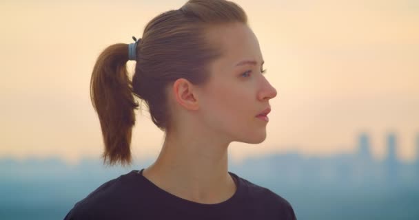 Retrato de cerca de una joven jogger femenina bastante deportiva en una camiseta negra mirando el hermoso atardecer al aire libre — Vídeos de Stock