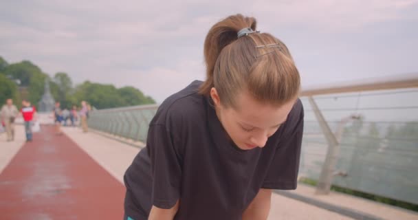 Retrato de primer plano de una joven atleta caucásica en una camiseta negra motivándose y empezando a correr en el puente en la ciudad urbana al aire libre — Vídeos de Stock