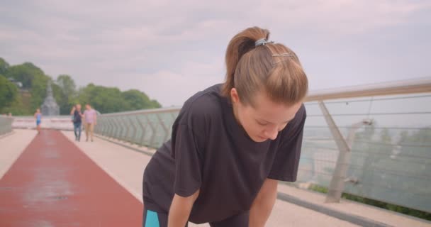 Primer plano retrato de joven linda deportista femenina en una camiseta negra motivándose y empezando a correr en el puente en la ciudad urbana al aire libre — Vídeos de Stock