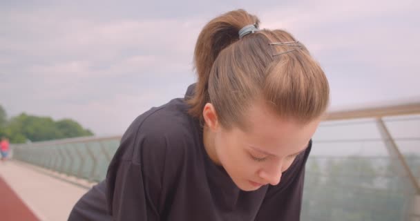 Retrato de close-up de jovem jogger feminino desportivo alegre em uma camiseta preta ficando motivado e começando a correr na ponte na cidade urbana ao ar livre — Vídeo de Stock