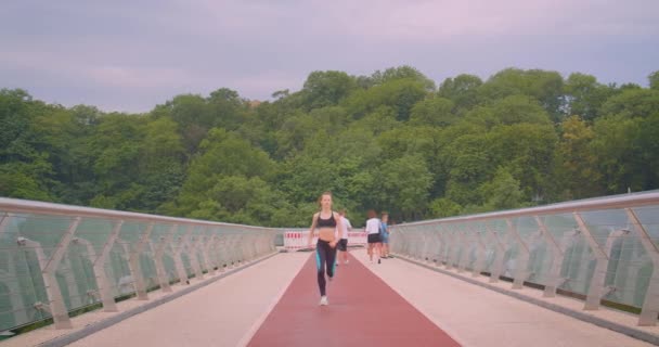 Closeup front view portrait of young pretty sporty female jogger running on the bridge in urban city outdoors — Stock Video