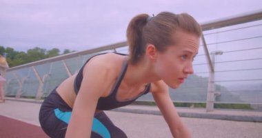 Genç belirlenen beyaz sportif kadın Jogger bir başlangıç pozisyonunda oturan ve kentsel şehir açık havada köprüde çalışan bir çekim yan görünüm portre