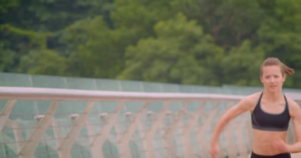 Closeup front portrait of young determined sporty female runner jogging with high speed on the bridge in urban city outdoors — Stock Video