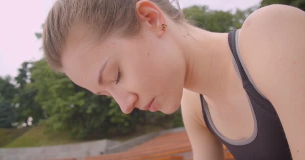 Closeup pohled na portrét mladé kavkazské sportovní sportovkyně, která je vyčerpaná a sedí na lavičce v městském městě — Stock video