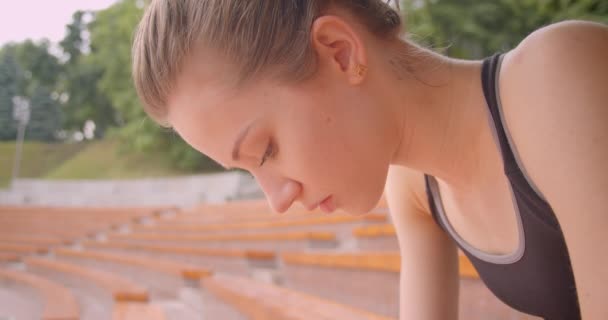 Closeup pohled na portrét mladé kavkazské sportovní sportovkyně, která se unavuje pohledem na fotoaparát s odhodláním sedět na lavičce v městském městě — Stock video