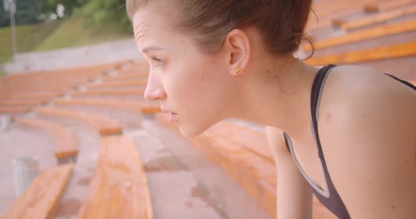 Closeup vista lateral retrato de jovem caucasiano atleta feminino desportivo olhando para a câmera com determinação sentado no banco na cidade urbana ao ar livre — Vídeo de Stock