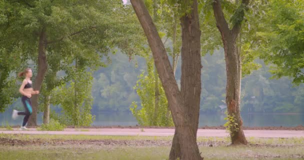 Närbild sida Visa porträtt av unga ganska sportig kvinnlig löpare jogging i parken i urbana staden utomhus — Stockvideo