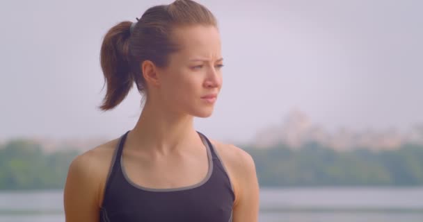 Retrato de primer plano de la joven jogger bastante femenina en ropa deportiva mirando hacia adelante con el cielo azul en el fondo al aire libre — Vídeos de Stock