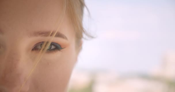 Closeup half face portrait of young cute caucasian female face with eye looking at camera with smiling expression outdoors — Stock Video