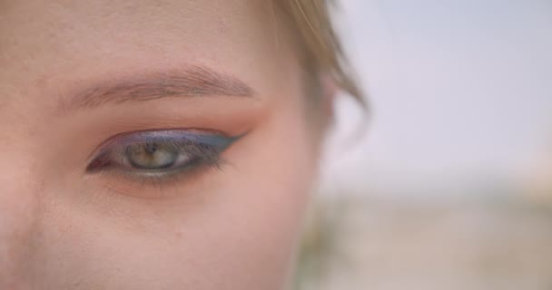 Closeup half face portrait of young charming blonde caucasian female face with eye looking at camera outdoors — Stock Video