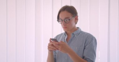 Ofiste kapalı telefon ayakta kullanarak Gözlük Genç yakışıklı beyaz işadamı bir portre