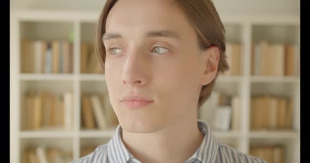 Close-up portret van jonge aantrekkelijke Kaukasische mannelijke student kijken naar camera in de bibliotheek binnenshuis — Stockvideo