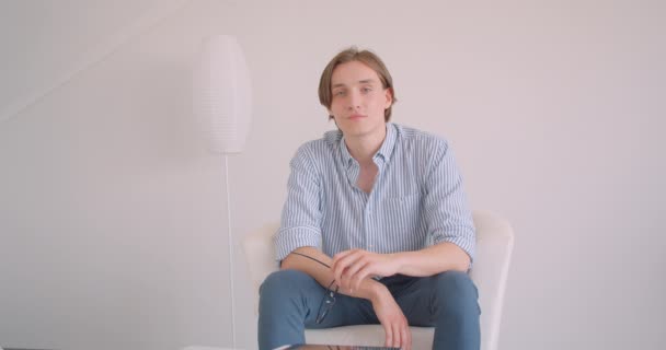 Closeup portrait of young attractive caucasian businessman looking at camera smiling happily sitting in the armchair indoors — Stock Video