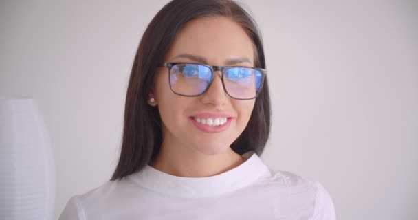 Primer plano retrato de la joven mujer de negocios bastante caucásica en gafas mirando a la cámara sonriendo felizmente con fondo blanco — Vídeos de Stock