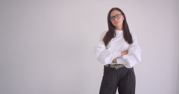 Портрет крупным планом молодой довольно кавказской предпринимательницы в очках со скрещенными руками на груди, смотрящей в камеру на белом фоне — стоковое видео
