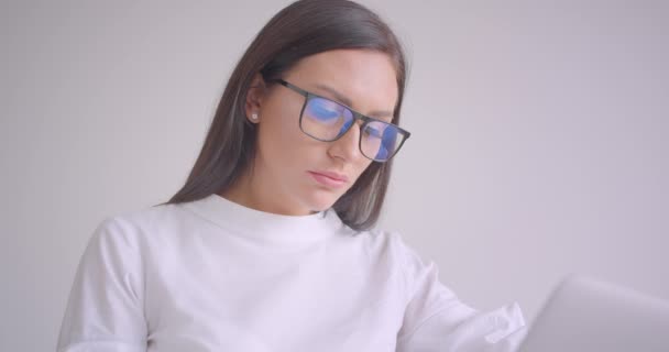 Retrato de cerca de la joven mujer de negocios bastante caucásica en gafas usando el portátil sentado en el sillón en la oficina blanca — Vídeos de Stock