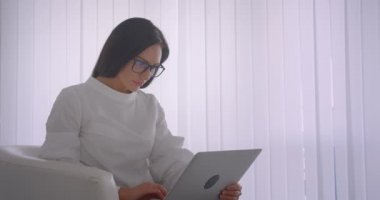 Gözlük Genç güzel beyaz işkadını fotoğraf makinesi görünümlü dizüstü bilgisayar kullanarak çekim yan görünüm portre neşeli koltukta oturuyor