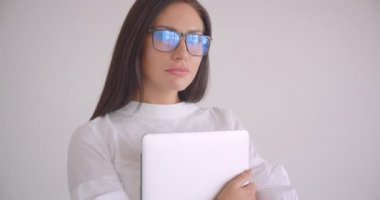 Beyaz ofiste güvenle ayakta kamera bakarak bir laptop tutan Gözlük Genç güzel beyaz işkadını portre closeup