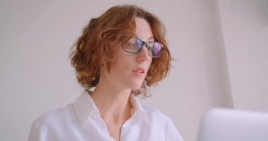 Beyaz ofiste koltukta otururken mutsuz olan dizüstü bilgisayar kullanarak gözlük yetişkin kızıl saçlı kafkas iş kadının Closeup portre