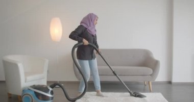 Elektrikli süpürge kullanarak ve daire içinde ev işleri yapıyor hijab genç Müslüman kadının Closeup portre