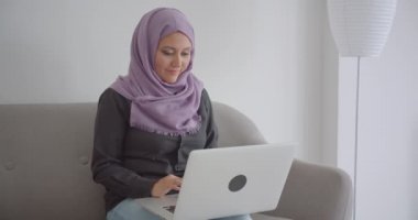 Dairede kapalı kanepede oturan dizüstü bilgisayar kullanarak hijab genç Müslüman iş kadını Closeup portre