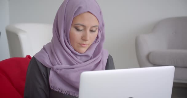 Zbliżenie portret młodego muzułmańskiego bizneswoman w hidżab za pomocą laptopa siedzi w torbie siedzącej patrząc na aparat uśmiechnięty wesw pomieszczeniu w mieszkaniu — Wideo stockowe